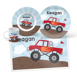 May include: A dinnerware set including a mug, a bowl, and a plate, plus a rectangular placemat. Each item features a red monster truck with flame decals, a red flag, and the name Keagan printed on a light blue background with white clouds.