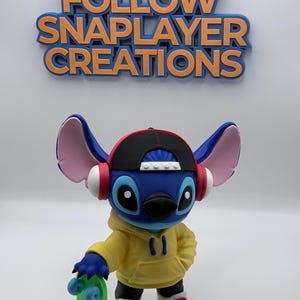 May include: A blue Stitch figurine wearing a yellow hoodie, black and red cap, and headphones, holding a green skateboard. The figurine has white sneakers with red accents. The text "FOLLOW SNAPLAYER CREATIONS" is above.