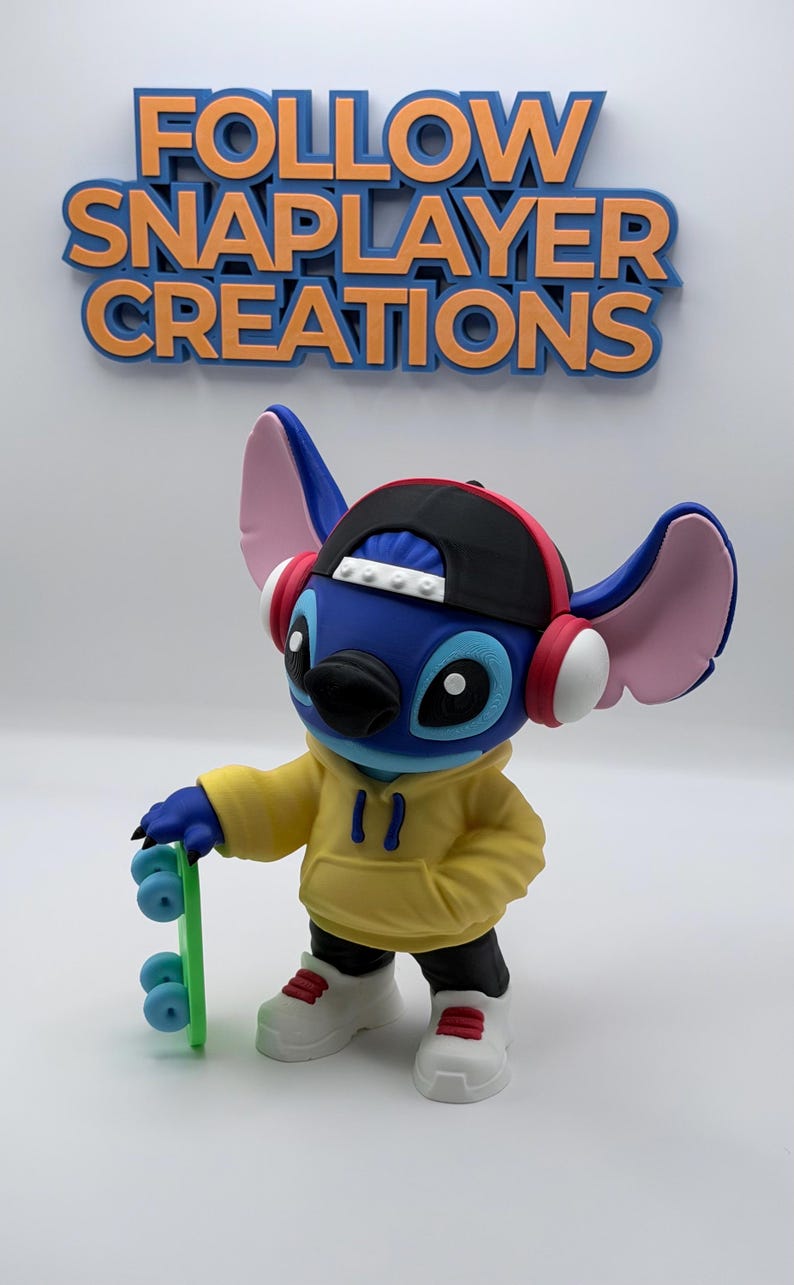 May include: A blue character figure wearing a black cap, yellow hoodie, and white sneakers, holding a green skateboard. The figure has pink ears and red headphones. The text "FOLLOW SNAPLAYER CREATIONS" is above the figure.