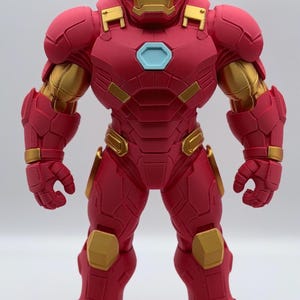 May include: A standing Iron Man action figure featuring a matte red and metallic gold armored suit. The character has a light blue hexagonal chest piece, a gold faceplate, and a robust, segmented design with visible 3D printed texture lines.