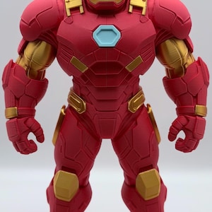 May include: A standing Iron Man action figure featuring a red and gold armored suit with a hexagonal light blue chest piece. The figure displays a detailed mechanical design with layered plating, a helmet with a gold faceplate, and articulated limbs.