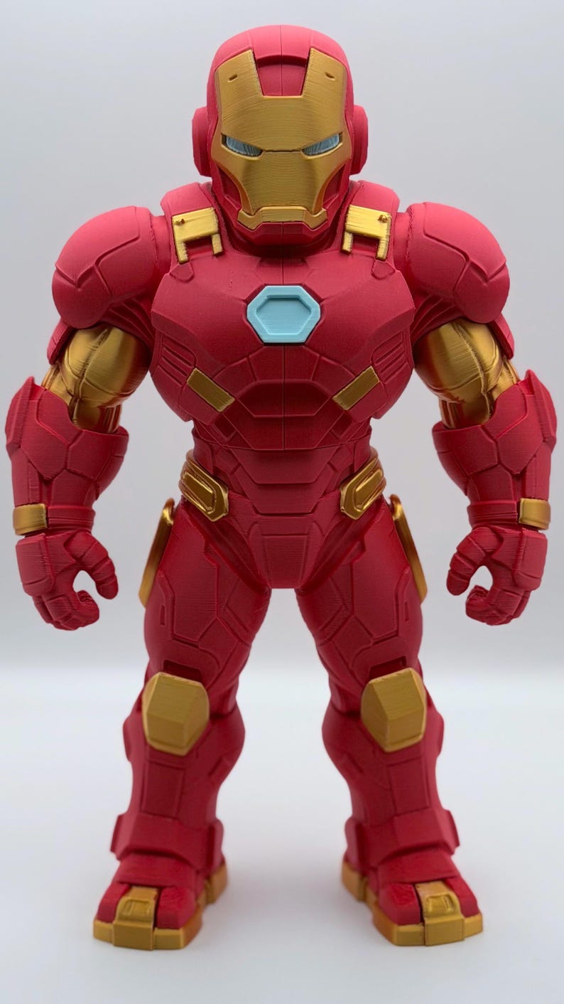 May include: A standing Iron Man action figure featuring a red and gold armored suit with a hexagonal light blue chest piece. The figure displays a detailed mechanical design with layered plating, a helmet with a gold faceplate, and articulated limbs.