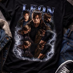 May include: Black t-shirt featuring a graphic of Leon Kennedy with multiple images of him and the text "LEON Kennedy" in a blue, metallic font. The design includes lightning effects. The shirt is surrounded by denim and sneakers.