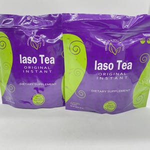 Pode incluir: Duas embalagens roxas e verdes do suplemento diet&eacute;tico "laso Tea". As embalagens t&ecirc;m uma parte superior roxa e um design de redemoinho verde na frente. O texto "laso Tea ORIGINAL INSTANT" &eacute; impresso em branco. As embalagens est&atilde;o em um fundo branco.