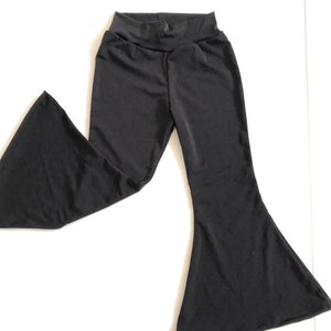 May include: Black flared pants with a high waistband. The pants are made of a smooth, stretchy fabric. The bell bottoms are wide and flowy, creating a retro silhouette. The pants are laid flat on a white surface.