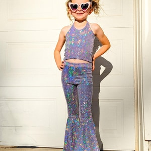 May include: A young person wearing a purple iridescent halter top and matching bell bottom pants. The outfit is covered in sequins and has a holographic effect. The person is wearing heart-shaped sunglasses and has their hair pulled back in a ponytail.