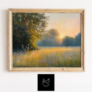May include: A framed landscape painting depicts a sunlit field with tall grass and wildflowers. The artwork features a golden-yellow and green color palette, with a soft, hazy atmosphere. The frame is a light gold color.