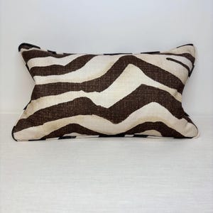 May include: Rectangular cushion with a zebra stripe design. The cushion has alternating brown and cream-coloured stripes. The item has a neutral colour scheme and is likely used for home decor.