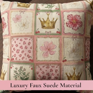 May include: A square throw pillow featuring a grid pattern of decorative squares. Each square contains illustrations of gold crowns, pink flowers, red cherries, and pink leopard print patterns. The fabric has a soft, textured appearance.