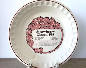 May include: A round, off-white ceramic pie dish with a fluted rim and a brown line border. The center features a graphic of pink strawberries and the text Strawberry Glazed Pie, along with a printed recipe listing ingredients and instructions.