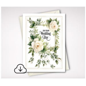 May include: A rectangular greeting card featuring a watercolor illustration of white roses and green foliage arranged in a frame. The text ON YOUR WEDDING DAY is printed in black script in the center. The card is placed on top of a white envelope.
