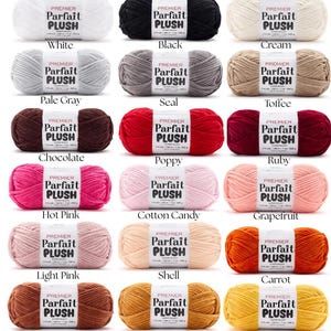 May include: A collection of Premier Parfait Plush yarn in various colors, including white, black, and cream. Each skein is labeled with its color name. The image showcases a range of hues, from pale gray to ruby, and rust to summer squash.