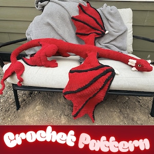 Pode incluir: Um grande dragão de pelúcia feito de crochê com um corpo vermelho vibrante, asas com bordas pretas e detalhes brancos na cabeça. A criatura tem uma cauda longa e fina e asas detalhadas. O texto "Crochet Pattern" é visível na parte inferior.