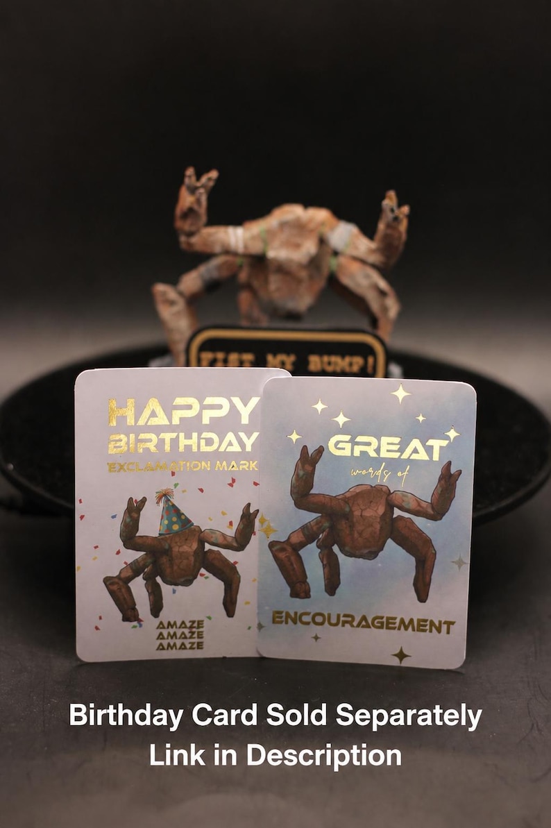 May include: Two rectangular greeting cards with gold foil text. The left card reads HAPPY BIRTHDAY EXCLAMATION MARK with a crab wearing a party hat. The right card reads GREAT words of ENCOURAGEMENT with a crab and gold star accents.