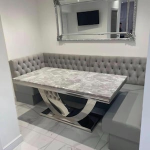 Puede incluir: Un moderno juego de comedor con una mesa rectangular con efecto mármol y una base cromada pulida. Incluye un banco gris con botones incorporado y asientos a juego. Un gran espejo adornado cuelga encima.