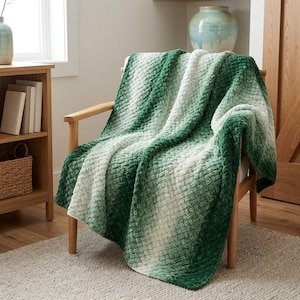 May include: A soft, textured throw blanket featuring a diagonal ombre gradient pattern that transitions from deep forest green to light sage and white. The fabric has a raised, woven-like appearance with a plush, velvety finish draped over a chair.