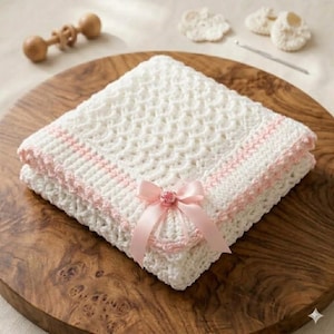 May include: A square white crocheted blanket featuring a textured wave pattern and a light pink crocheted border. The blanket is adorned with a light pink satin ribbon tied into a bow at the centre of one edge, featuring a small decorative floral accent.