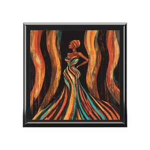 Könnte beinhalten: Gerahmter Kunstdruck mit einer stilisierten Illustration einer Frau in einem fließenden Kleid. Das Kleid ist mit orangefarbenen, türkisfarbenen und gelben Streifen versehen. Der Hintergrund hat vertikale wellenförmige Linien in Orange und Braun. Die Frau trägt ein passendes Kopftuch.