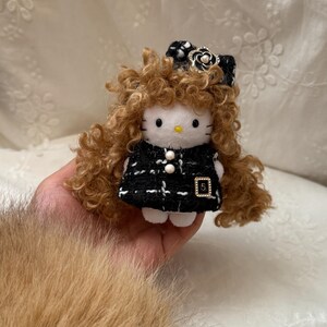 Könnte beinhalten: Plüsch-Hello Kitty-Puppe mit lockigem braunem Haar und einem schwarz-weißen Tweed-Outfit. Die Puppe hat eine schwarze Schleife mit Perlenakzent und ein kleines goldenes Quadrat mit der Nummer 5.