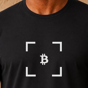 Könnte beinhalten: Ein schwarzes T-Shirt mit kurzen Ärmeln und einer weißen Grafik auf der Brust. Die Grafik besteht aus einem zentralen Bitcoin-Symbol, das von vier weißen Eckklammern umschlossen ist und einen Rahmeneffekt erzeugt. Der Stoff ist durchgehend schwarz.