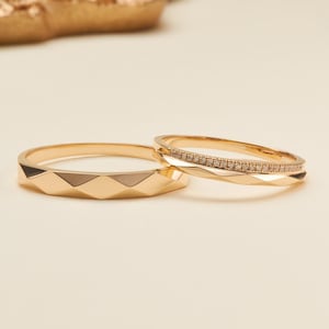 Puede incluir: Dos anillos de oro se muestran. Un anillo presenta un diseño de banda geométrica facetada. El segundo anillo es más delgado, con una banda facetada en un lado y una fila de pequeñas piedras redondas transparentes incrustadas en la parte superior.
