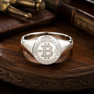 以下が含まれることがあります： ビットコインのシンボル、LIBERTAS AEQUITAS VERITASの文字、2009年、無限大の記号、そして中央のアイコンを囲むIN CRYPTOGRAPHY WE TRUSTのフレーズが刻印された円形のフェイスを持つ、磨き上げられたシルバーのシグネットリング。