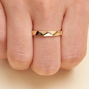 May include: A polished rose gold band ring featuring a faceted, geometric surface design. The ring has a smooth, reflective finish with a series of angled planes that create a subtle mountain-like peak pattern across the center of the band.