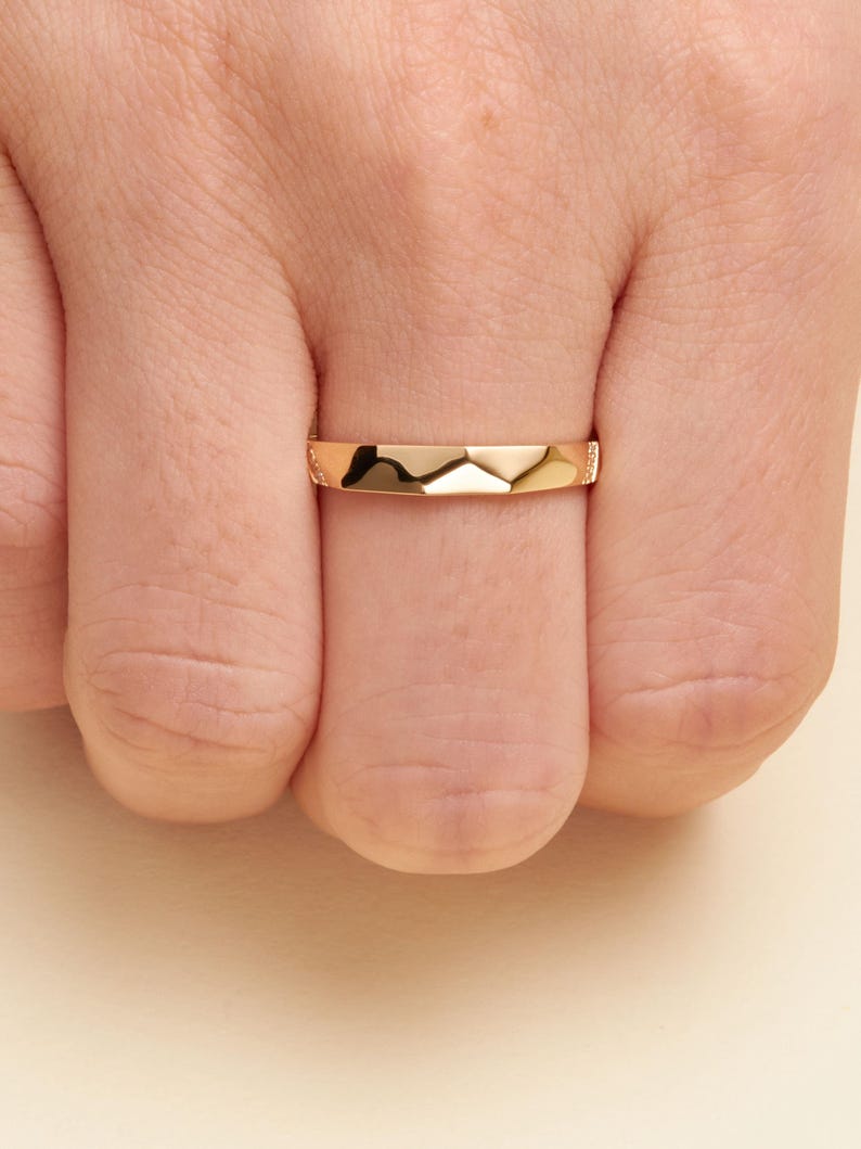 May include: A polished rose gold band ring featuring a faceted, geometric surface design. The ring has a smooth, reflective finish with a series of angled planes that create a subtle mountain-like peak pattern across the center of the band.