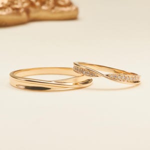 May include: Two gold rings with a twisted design. One ring features a smooth, polished gold surface, while the other ring has a matching twisted band set with a row of small, clear, sparkling stones along the top half of the circular band.