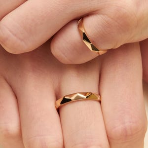 May include: Two polished gold rings with a faceted, geometric surface design. Each ring features a series of angular, flat planes that create a multi-faceted appearance, reflecting light across the metallic surface of the bands.
