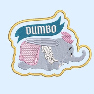 以下が含まれることがあります： 象のダンボが描かれた刺繍ワッペン。灰色の象はピンクの帽子とピンクと灰色の毛布を身に着けています。「Dumbo」の文字が象の上に青いバナーで書かれており、すべて金色の縁取りの中にあります。