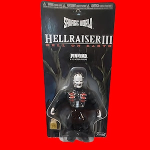 Puede incluir: Una figura de acción de Pinhead de Hellraiser III, empaquetada en una tarjeta negra y gris. La figura es negra con detalles rojos y una cara pálida con alfileres. El embalaje dice "SAVAGE WORLD HELLRAISER III HELL ON EARTH PINHEAD 5 1/2 ACTION FIGURE Funko."