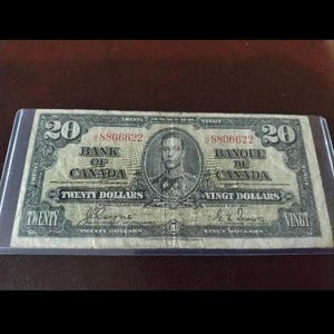 Op de afbeelding: Een twintig dollar biljet van de Bank of Canada, met serienummer 8806622. De biljet toont een portret van een man en de tekst "Twenty Dollars" in het Engels en Frans. De biljet wordt beschermd door een transparante plastic hoes.