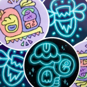 May include: A collection of colorful, round stickers with unique, whimsical designs. The stickers feature neon blue outlines and vibrant pastel colors, including pink, yellow, and purple. Some designs have a cartoonish style, while others have a more abstract appearance.