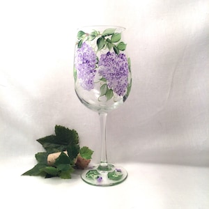 May include: A clear glass wine glass with a hand-painted design of purple hydrangeas and green leaves.