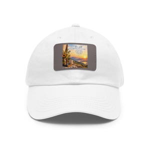 Peut inclure: Une casquette de baseball blanche avec un écusson rectangulaire sur le devant. L'écusson présente un paysage avec un lever de soleil sur des montagnes, un bouquet de tournesols, une tasse de café et un livre, avec le texte Be still and know that I am God.