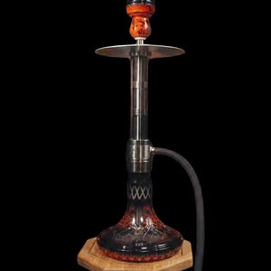 May include: A contemporary hookah with a dark red glass base and a stainless steel stem. The hookah has a black hose and a wooden base. The top features a decorative, multi-colored top. The hookah is designed for smoking.