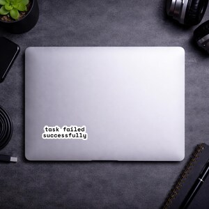 May include: A white ceramic mug with a black handle and the text "But First, Coffee" in a black, handwritten-style font. The mug is on a white surface.