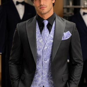 May include: A dark charcoal grey suit jacket with satin lapels worn over a black dress shirt and a light lavender paisley patterned waistcoat. The ensemble includes a matching lavender paisley necktie and a coordinating pocket square in the breast pocket.