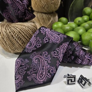 Peut inclure: Ensemble de cravate, pochette et boutons de manchette noirs avec un motif cachemire violet. Les boutons de manchette carrés présentent un motif géométrique noir et argent. L'ensemble est présenté avec de la ficelle et des citrons verts.