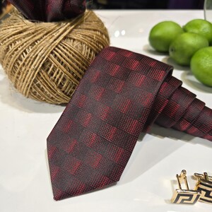 May include: A burgundy tie with a checkered pattern, a matching pocket square, and gold cufflinks with a black geometric design. A ball of twine and green limes are in the background.