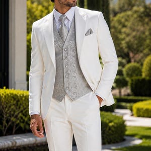 May include: A white suit jacket and matching trousers paired with a white dress shirt, a silver paisley patterned waistcoat, a matching silver paisley necktie, and a silver paisley pocket square tucked into the jacket breast pocket.