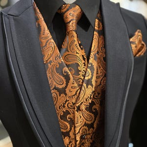 May include: A black suit with a black shirt, and a paisley patterned waistcoat, tie, and pocket square. The paisley design is gold and black. The suit is displayed on a mannequin.