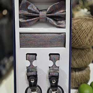 May include: A formal wear set in a box, featuring a bow tie, cummerbund, and suspenders. The set has a shimmering, multicolored fabric with black leather suspender ends and silver-tone hardware. The bow tie is pre-tied.