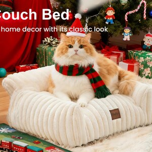 May include: A ginger and white cat wearing a Santa hat and a red and green scarf, resting on a cream-coloured, corduroy-textured pet bed. The bed has a small brown label. The background includes a Christmas tree and wrapped gifts.