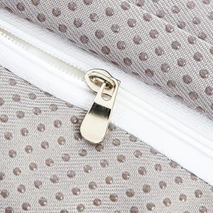May include: Close-up of a light grey fabric with small, evenly spaced, dark grey polka dots. A white zip runs diagonally across the image, with a gold-coloured metal zip pull.