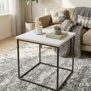 Puede incluir: Una mesa de centro cuadrada blanca con estructura de metal negro. Una taza de café, una pequeña suculenta y un libro están sobre la mesa. La mesa está sobre una alfombra peluda gris y blanca.