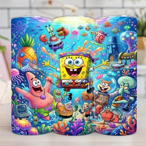 Op de afbeelding: Een kleurrijke beker met een levendige onderwaterwereld met stripfiguren. Het ontwerp bevat SpongeBob SquarePants, Patrick Star, Octo Tentakel en andere personages uit de animatieserie, tegen een blauwe en koraal achtergrond.