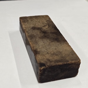 May include: A rectangular, brown whetstone with a textured surface. The sharpening stone is designed for honing blades and tools. The stone is approximately 4 inches long, 1.5 inches wide, and 1 inch thick.