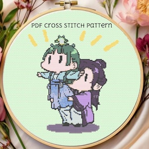May include: A cross-stitch pattern in a wooden hoop features two cartoon figures in traditional clothing. The figures are in shades of green, blue, and purple, with the text "PDF CROSS STITCH PATTERN" above them. The background is light green.